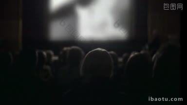 在电影院看电影的人的背影，离焦的屏幕，电影照亮了黑暗大厅里的观众